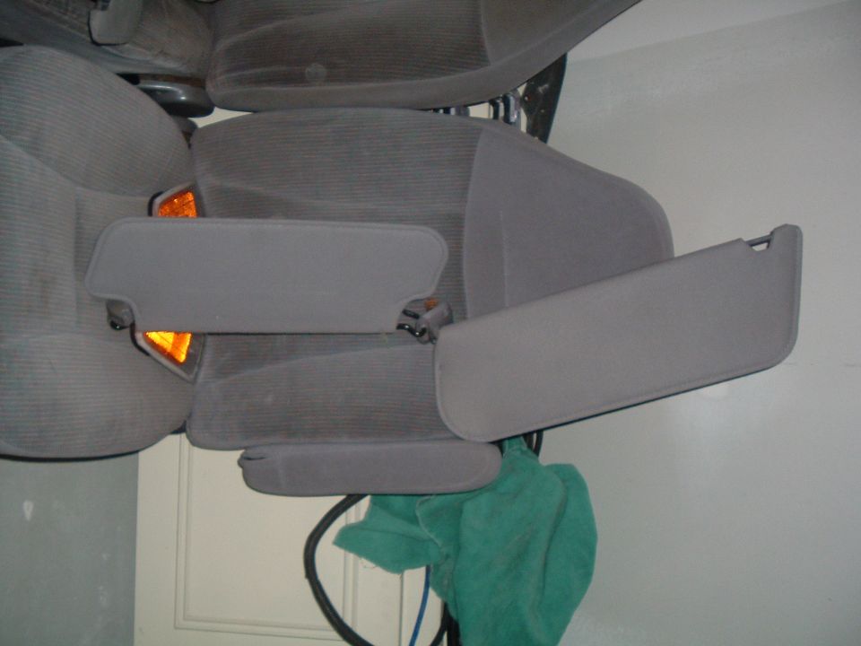 Car interior with gray fabric seats and folded-down sun visors. Orange interior light visible