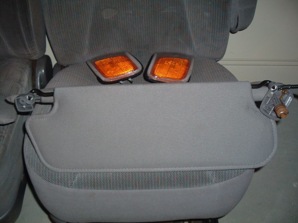 Two amber marker lights and a sun visor are resting on car seats