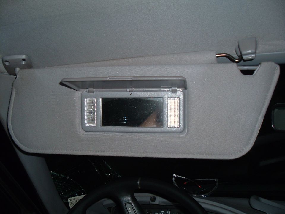 Interior shot of a car's sun visor with a mirror and lights. Steering wheel and dashboard visible below