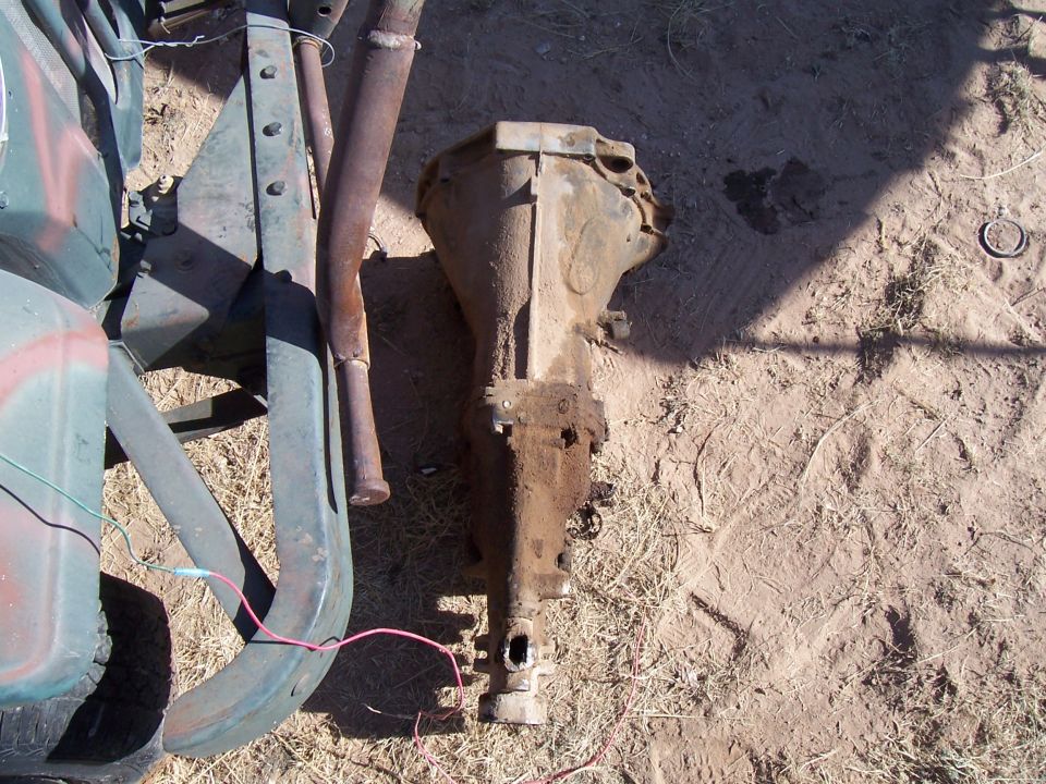 Rusted metal transmission housing and exhaust pipe on dirt ground