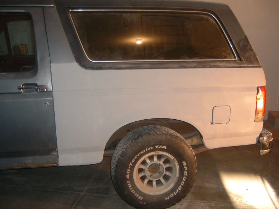 Gray and white Ford Bronco side view, showing primer on rear quarter panel and rust on lower door
