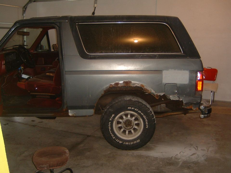 Gray Ford Bronco with rust damage on rear quarter panel and missing rear bumper section