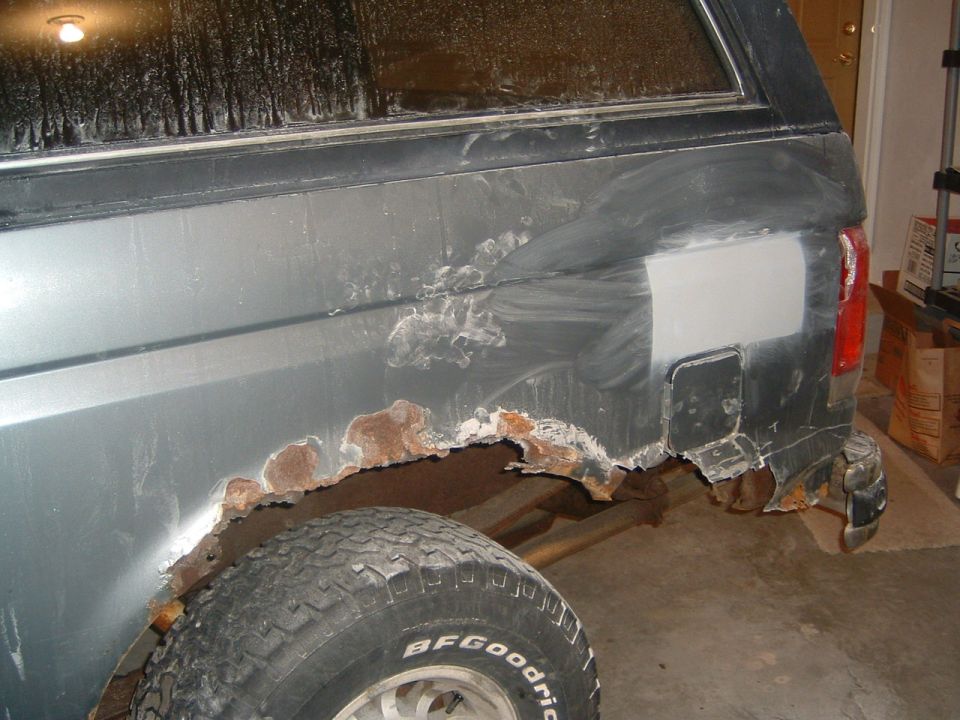 Rear passenger side of a Ford Bronco with significant rust damage and body filler applied
