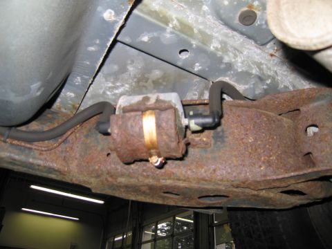 1991 Ford LTD Crown Victoria - Close-up view of a vehicle's underbody fuel filter, showing significant rust on the mounting bracket and surrounding frame components.
