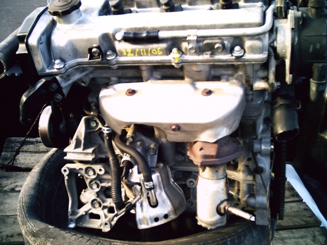 Engine block with exhaust manifold and various hoses attached, resting on a tire