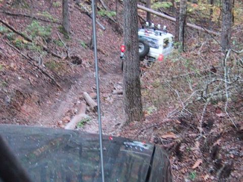 1995 Ford Bronco - A white 1995 Ford Bronco navigates a challenging, steep trail surrounded by trees in a wooded area.