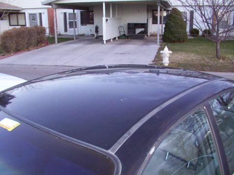 2003 Ford Ranger - A dark blue car's roof is visible in the foreground, with a residential driveway and house in the background.