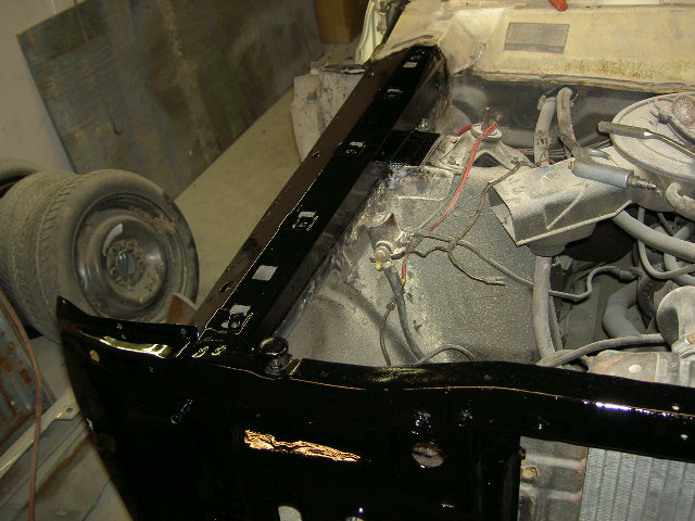Black painted vehicle frame and engine bay with visible wiring and a tire in the background