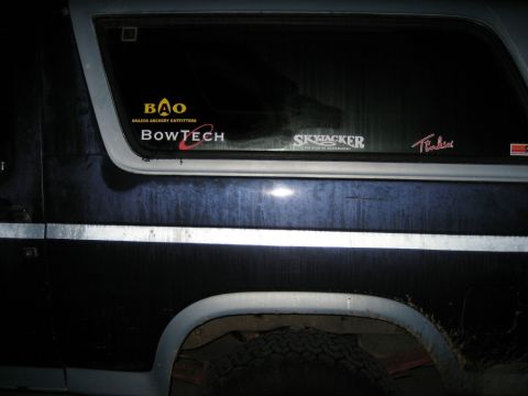 1986 Ford Bronco - Night close-up of the rear quarter panel and side window of a dark blue full-size SUV with a white bodyside stripe, white fender flare and…