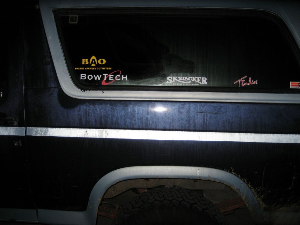 Dark blue SUV rear quarter window at night with BowTech, Skyjacker and Brazos Archery decals