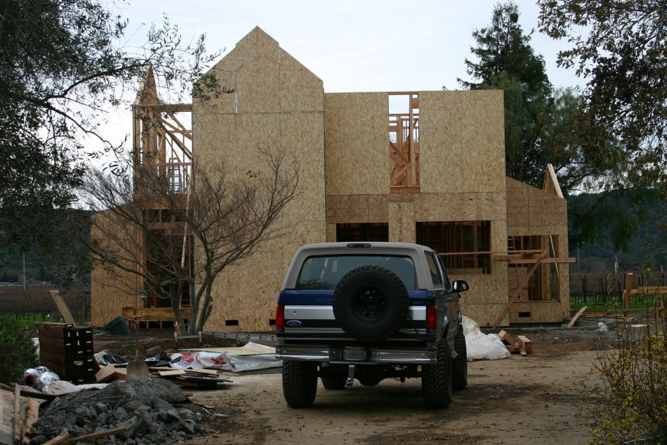1996 Ford Bronco parked in front of a house under construction. The vehicle is blue and grey with a spare tire mounted on the rear