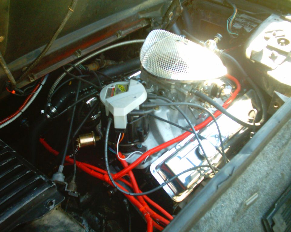 V8 engine in a Fiero engine bay with chrome air cleaner, chrome valve cover, red plug wires and white distributor cap