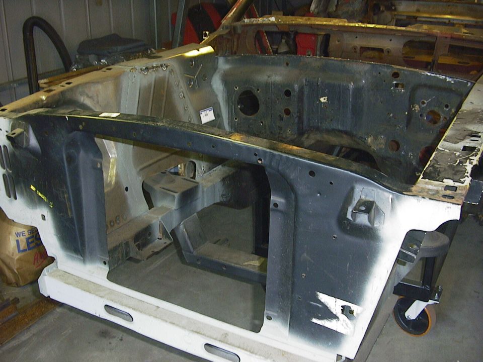Car frame showing engine bay structure with some black overspray and a white bumper section