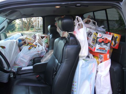 1995 Ford Bronco - The interior of a vehicle is filled with numerous shopping bags and toy boxes, suggesting a holiday toy drive or shopping trip.