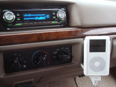 1996 Ford Bronco - Tan dash center stack fitted with an aftermarket Pioneer CD/MP3 head unit displaying "iPod0047" on its blue screen, a wood-grain trim strip…