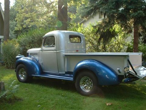 1946 Chevrolet C/K Pickup - A classic two-tone pickup truck sits in a grassy yard, bathed in sunlight filtering through the trees.