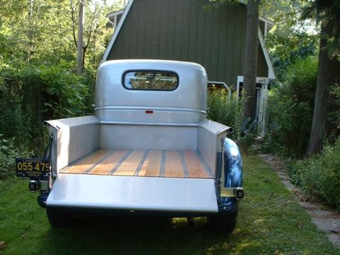 1946 Chevrolet C/K Pickup - A vintage pickup truck with a wooden bed is parked in a grassy area with trees and a building in the background.