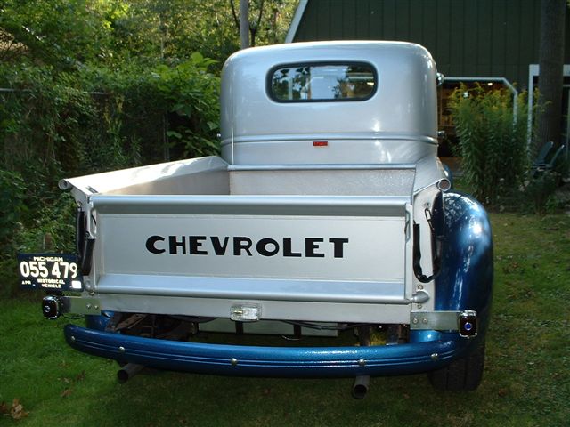 Silver Chevrolet pickup truck, rear view, with 'CHEVROLET' on tailgate, blue bumper, and Michigan license plate
