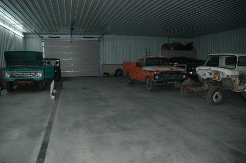 1963 Ford F-250 - Multiple trucks are parked inside a metal-sided garage with a large overhead door.
