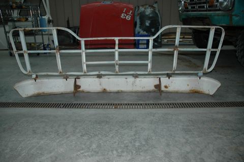 1963 Ford F-250 - A white grille guard and bumper assembly is shown in a workshop setting, with other vehicle parts in the background.