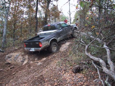 1995 Ford Bronco - Pickup truck navigates a challenging off-road trail through a wooded area.