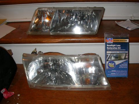 1998 Mercury Grand Marquis - A headlight restoration kit sits next to two car headlights on a wooden surface.