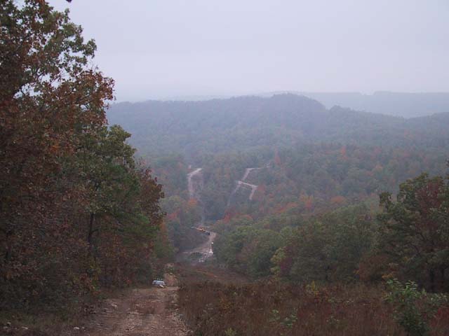 Hazy valley overlook from a dirt trail with off-road tracks cut across autumn wooded hills