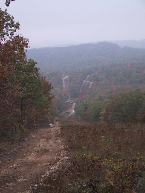1995 Ford Bronco - A white SUV is parked on a dirt road, surrounded by trees. A winding road is visible in the distance.