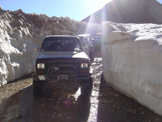 Jeep-like SUV with winch driving through a narrow path between tall snow walls
