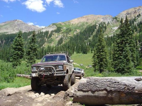 1986 Ford Bronco II - Several off-road vehicles navigate a challenging mountain path under a clear blue sky.