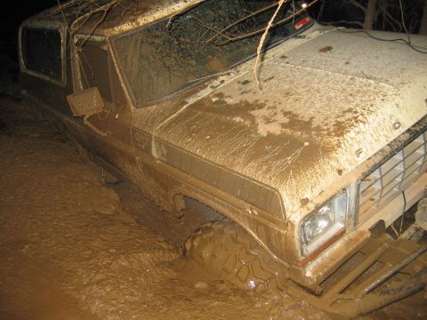 1992 Ford Mustang - A heavily mud-caked 1980 Ford Bronco is deeply mired in thick mud, with only its front end visible.