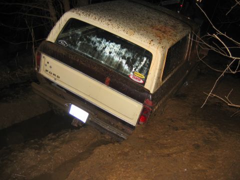 1992 Ford Mustang - A Ford Bronco is stuck in thick mud, viewed from the rear.