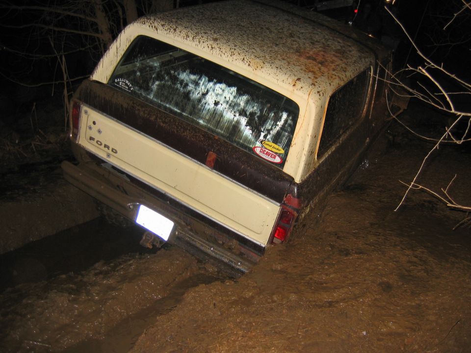 Brown and cream Ford Bronco stuck in mud, rear view