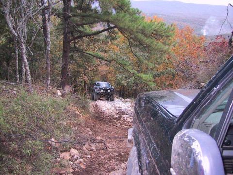 1995 Ford Bronco - Two SUVs navigate a challenging off-road trail through a wooded landscape during autumn.