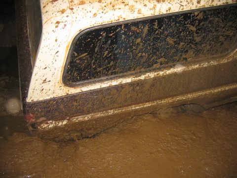 1992 Ford Mustang - A white vehicle is stuck deep in thick mud, with mud splattered across its side panel and window.