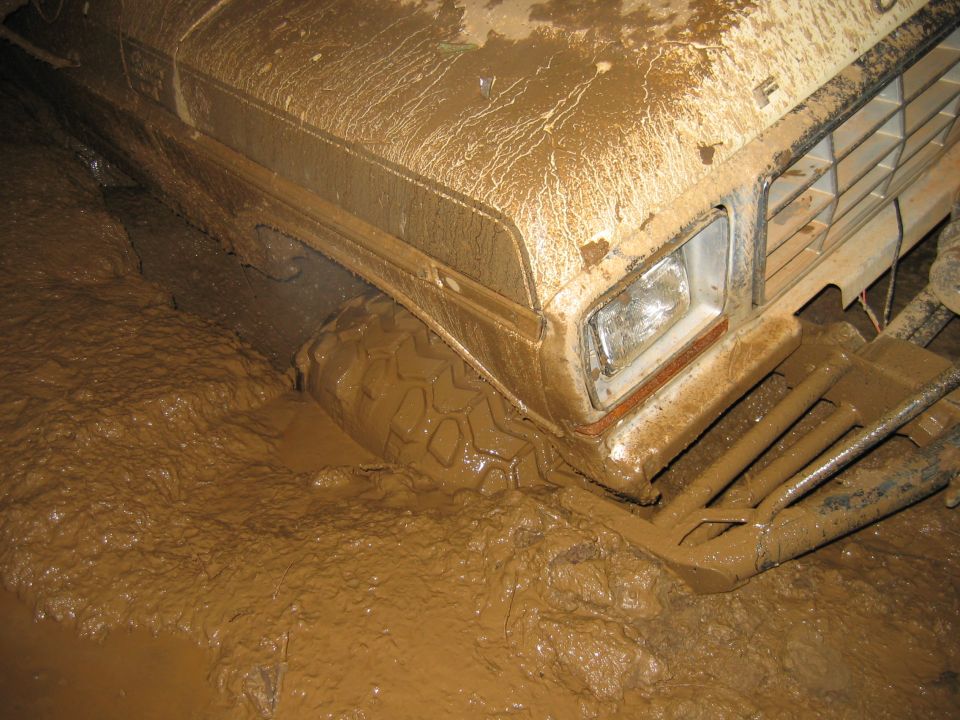 Ford truck front end stuck deep in thick mud, tire visible