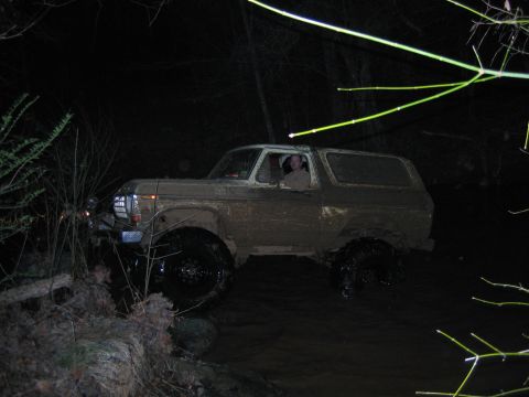 1992 Ford Mustang - A driver navigates a muddy off-road path at night in a large SUV.