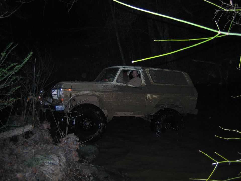 Muddy SUV driving through water at night. Driver visible