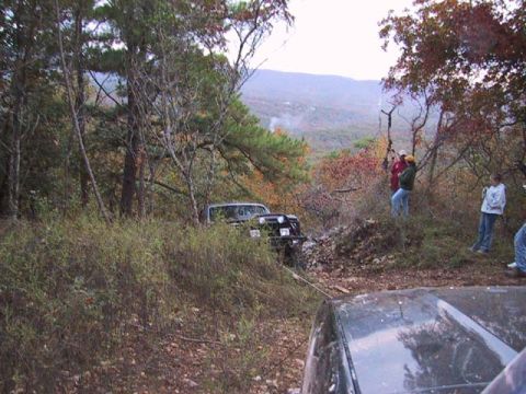 1995 Ford Bronco - A group of people and their off-road vehicles are gathered in a wooded area with hills in the background.