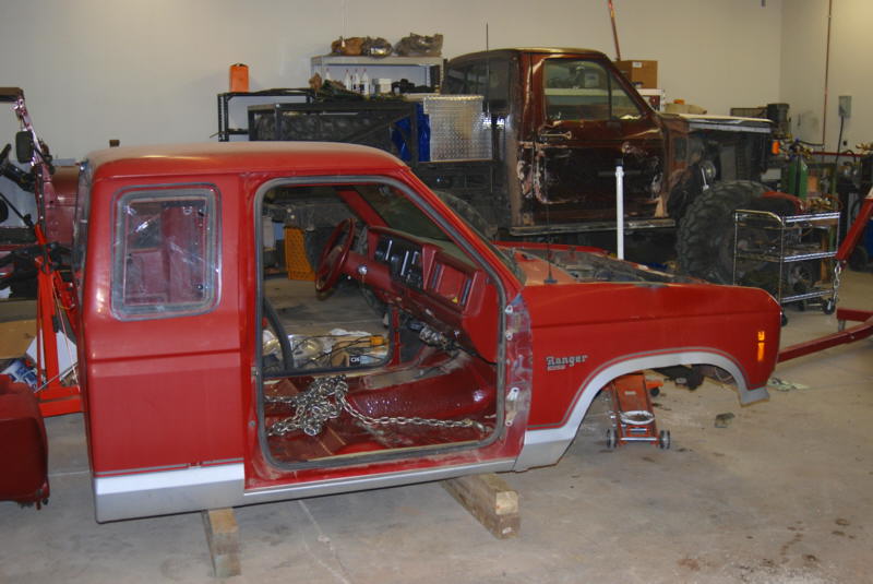 Red truck cab on wood blocks, stripped interior, in a garage