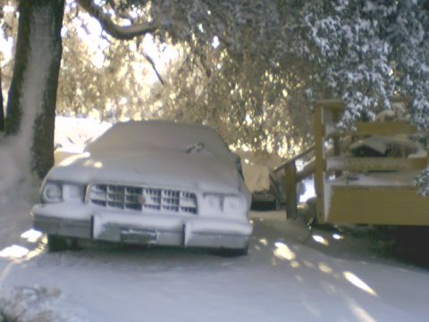 1973 Ford Ranchero - A 1973 Ford Ranchero sits covered in snow, with a wooden structure to its right.