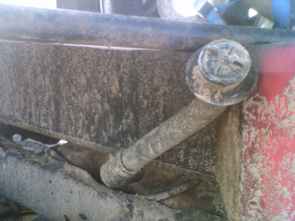 Rusty mud-caked suspension link bolted to a frame bracket under a truck