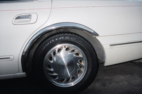 1989 Ford Bronco - Close-up of a white car's rear wheel well, showing the tire and alloy wheel with chrome fender trim.