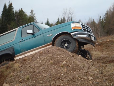 1996 Ford Bronco - Teal Ford Bronco with tan stripe climbing a dirt mound, front right wheel elevated.