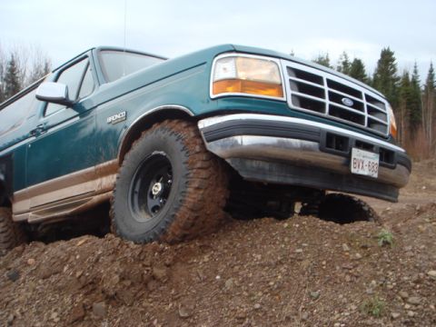 1996 Ford Bronco - A green 1996 Ford Bronco navigates an off-road terrain with mud-splattered tires.