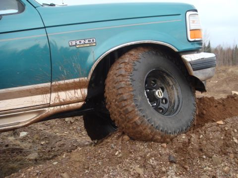 1996 Ford Bronco - A teal 1996 Ford Bronco with large off-road tires is stuck in a dirt ditch, showing its side profile.
