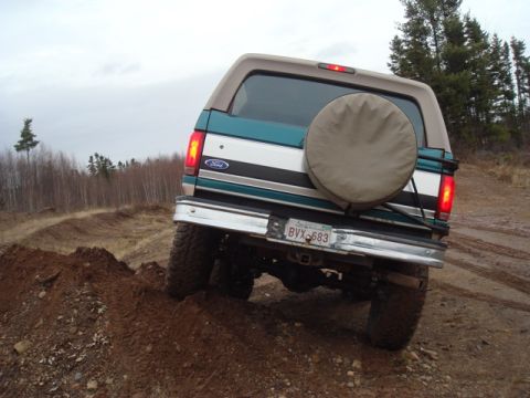 1996 Ford Bronco - The Ford Bronco navigates a muddy, off-road trail under an overcast sky.