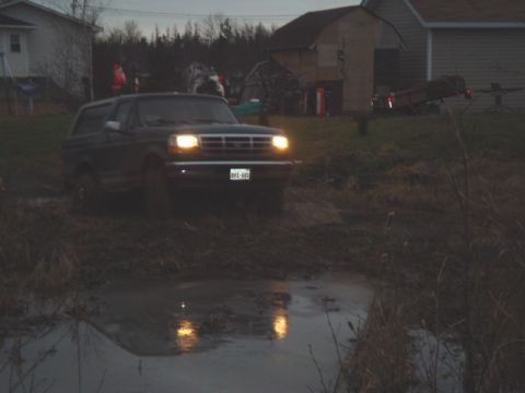 1996 Ford Bronco - 1996 Ford Bronco navigating a muddy terrain with headlights illuminated.