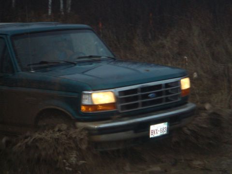 1996 Ford Bronco - A green Ford truck navigates through muddy terrain, its front grille and headlights visible.