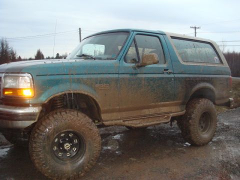 1996 Ford Bronco - This 1996 Ford Bronco is heavily covered in mud, indicating off-road use, with its side profile clearly visible.